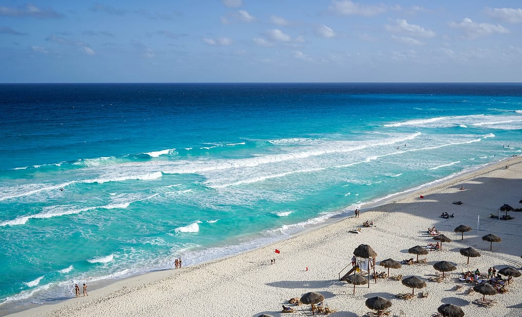 Beach with turquoise water and people on the sand under palapas