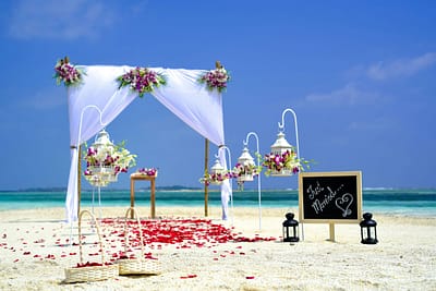 pexels-asad-photo-maldives-169196 A destination wedding or vow renewal on the beach in the Maldives. It shows the couple's archway decorated with tulle and flowers along with rose petals lining the walkway.