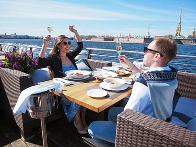 pexels-nadin-sh-78971847-12107003 Couple eating outside on the top deck of a cruise ship, overlooking the water.