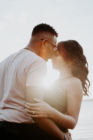 Man lovingly kissing woman on nose with sunset on the beach in the background.