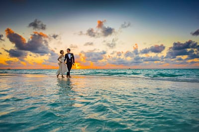 During sunset, the bride and groom walks through the ocean on the beach at the Maldives.