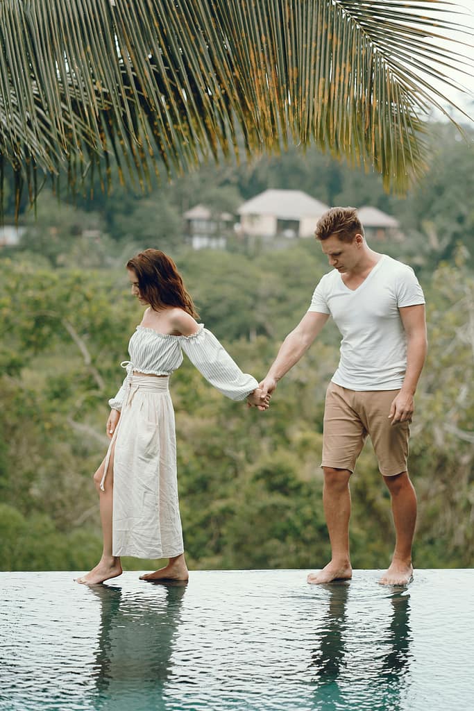 pexels-gustavo-fring-4172886 Man and woman walking along the edge of an infinity pool while holding hands with a jungle in the background.